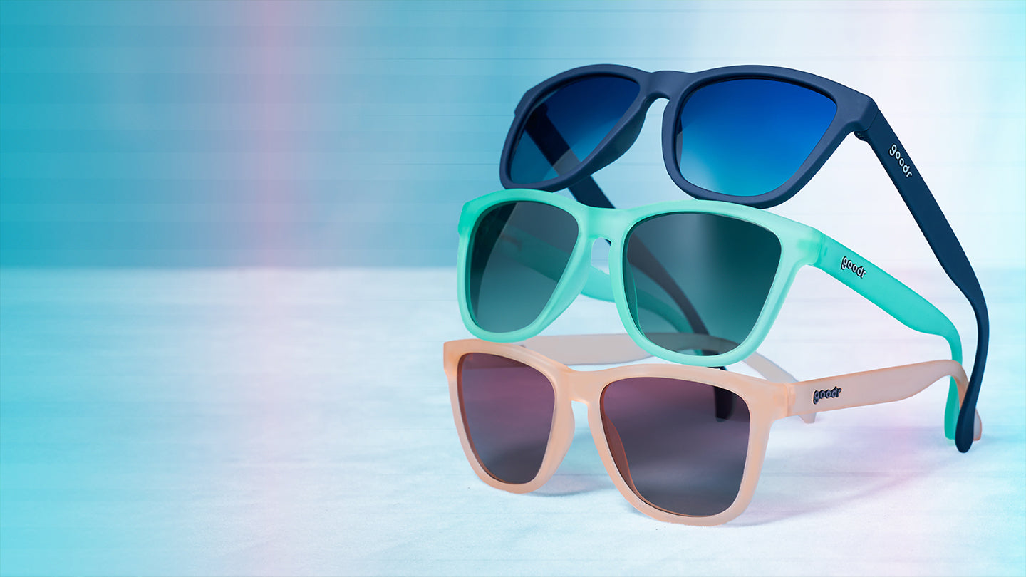 Three pairs of sunglasses stacked on top of one another, a pink pair, a green pair, and a navy blue pair.