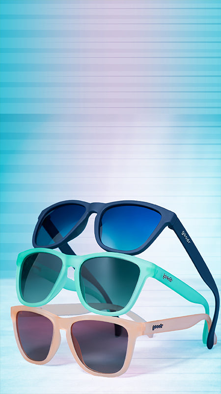 Three pairs of sunglasses stacked on top of one another, a pink pair, a green pair, and a navy blue pair.