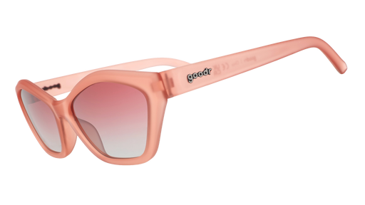 Three-quarter angle view of geometric sunglasses with translucent coral pink frames and gradient lenses against a white background.