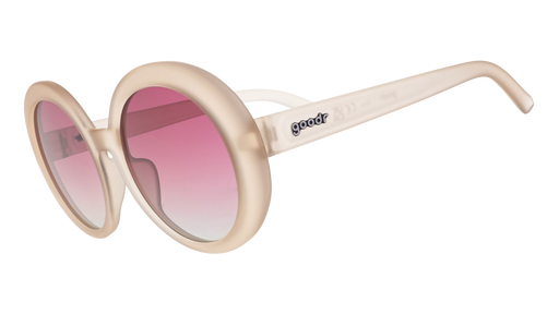 Three-quarter angle view of oversized round beige sunglasses with purple gradient lenses against a white background.