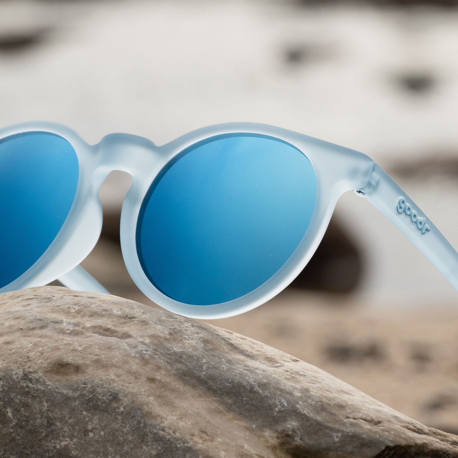 Close-up of translucent blue-gray Circle Gs with ice blue reflective lenses posing on a gray seaside rock.