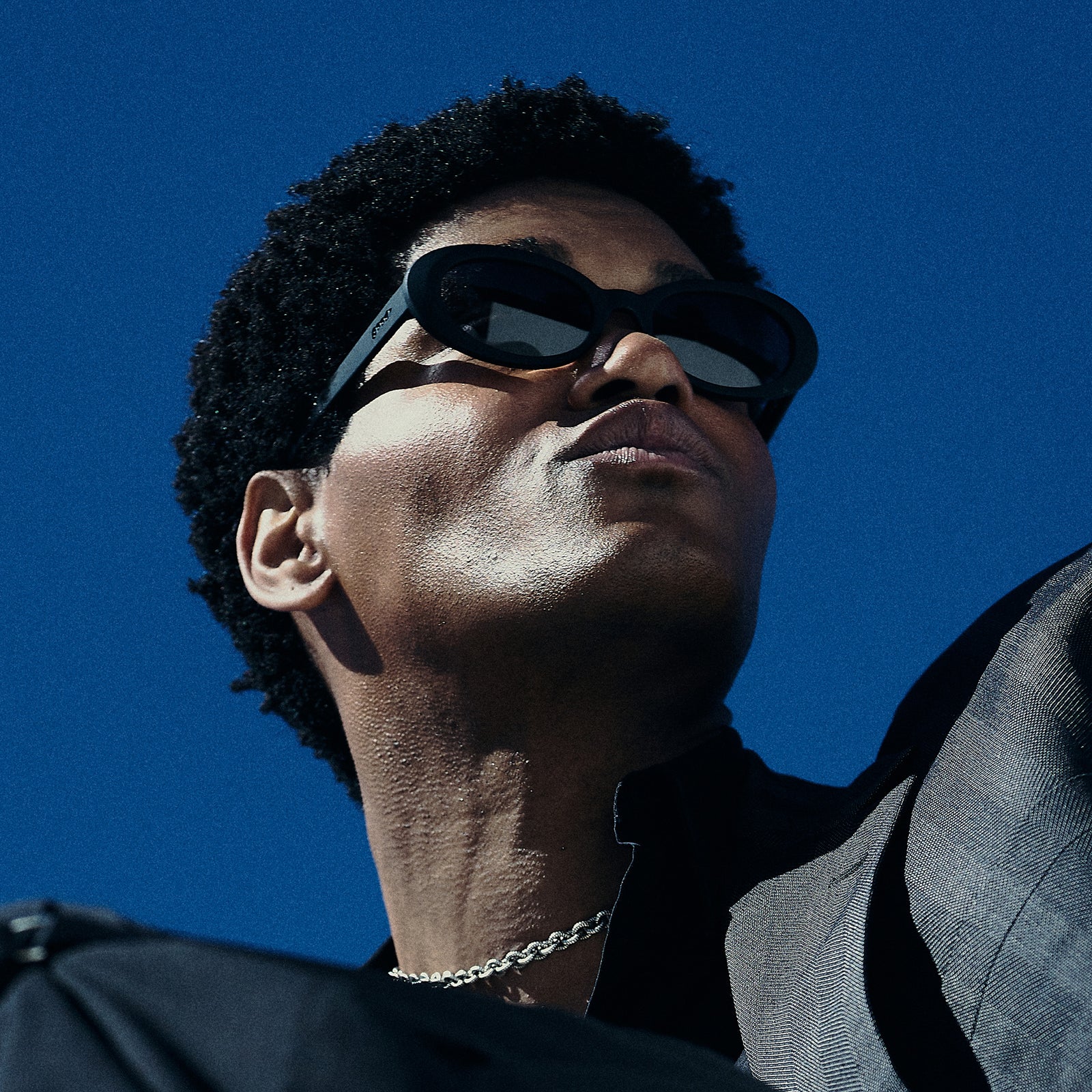 Low-angle view of a man wearing black oval sunglasses with polarized lenses against a white background.