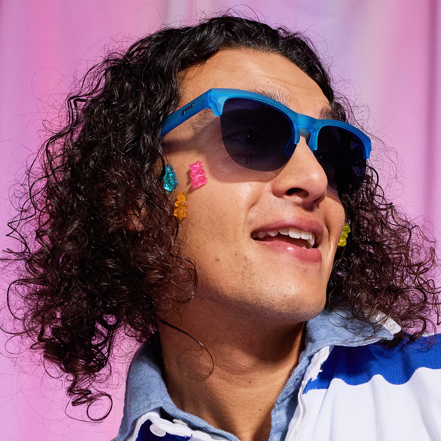 A man with dark curly hair and gummy bears stuck on his cheek wears translucent blue half-rim Avant G sunglasses.
