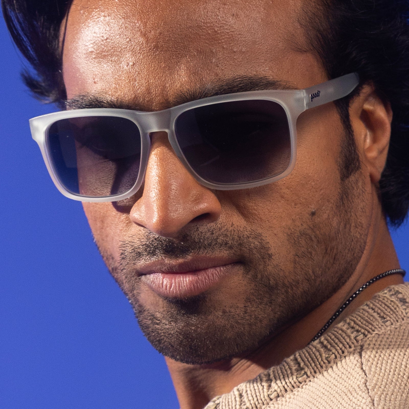 A stylish man with black wavy hair poses for the camera in translucent gray Grand Gs with black gradient lenses.