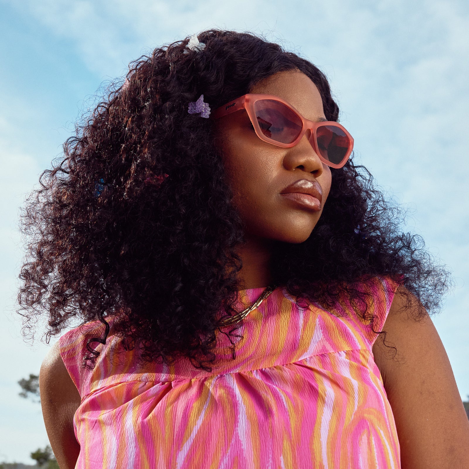 Side profile of a woman wearing geometric sunglasses with translucent coral pink frames and gradient lenses.
