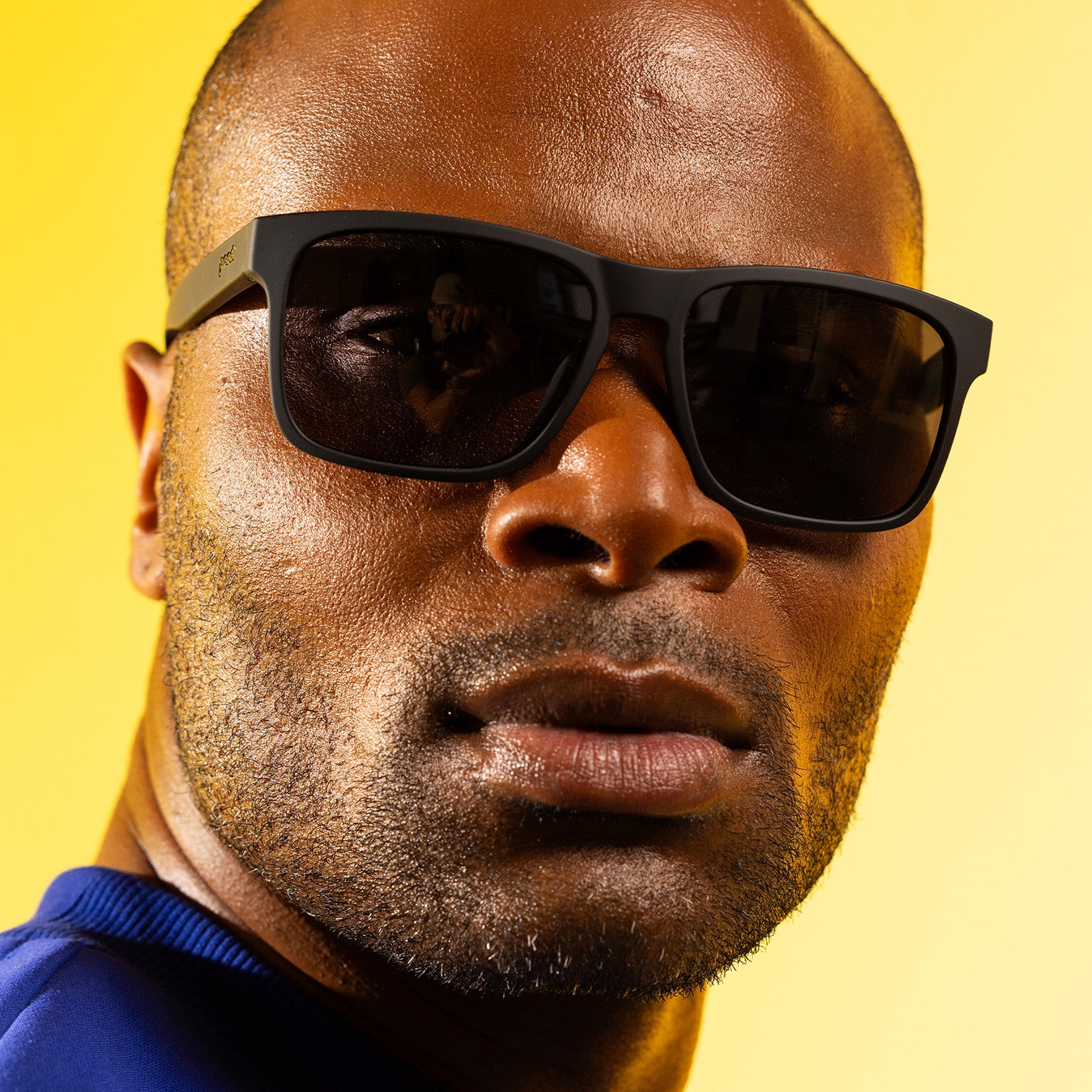 A stylish man with dark, cropped hair smirks at the camera in black Grand Gs with black non-reflective lenses.