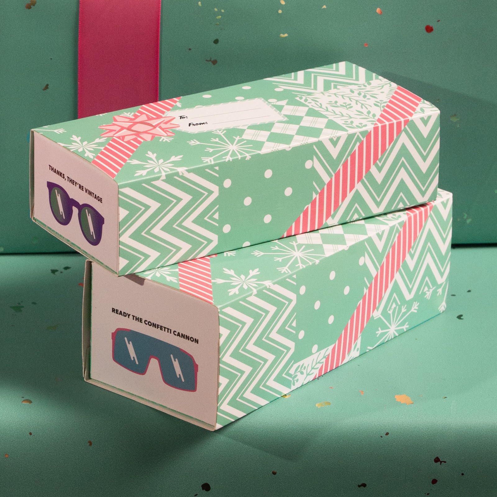 Three-quarter angle view of two goodr boxes slipped into teal holiday wrapping sleeves on a festive background.