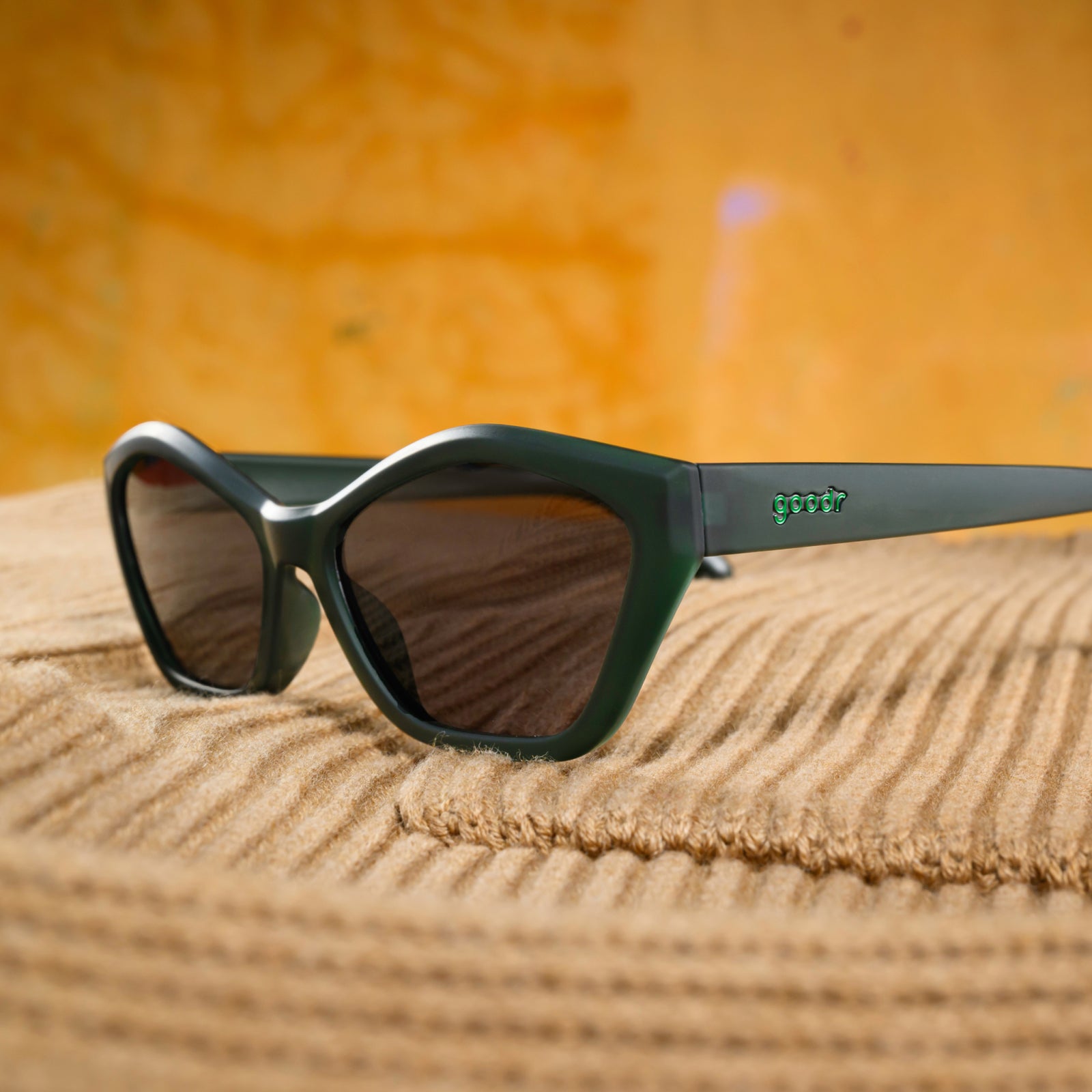 Three-quarter-angle view of translucent, dark green angular Deco G sunglasses sitting on a camel-colored sweater material.