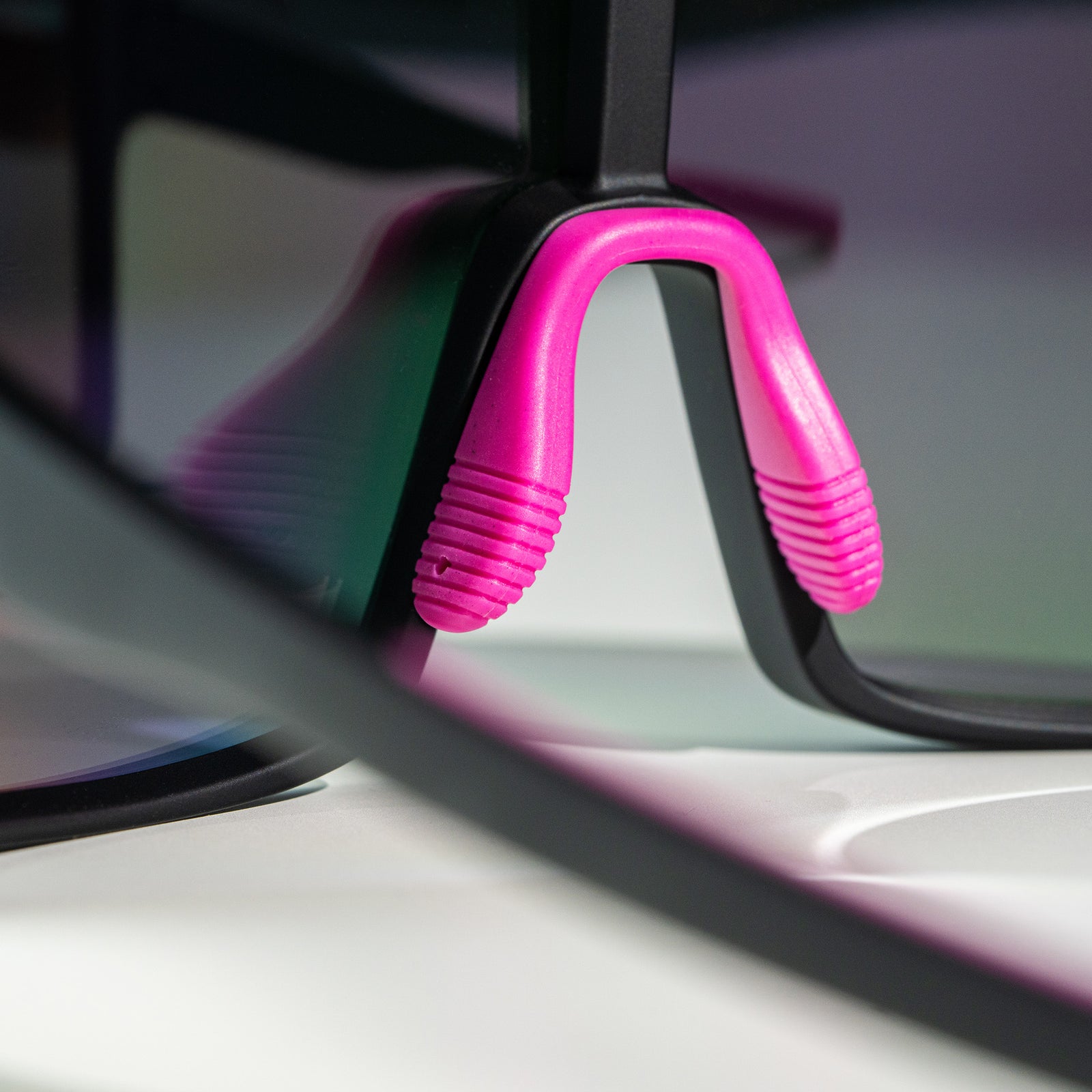 Close-up shot of a pair of black wrap sunglasses with a hot pink adjustable nosepiece photographed from behind.