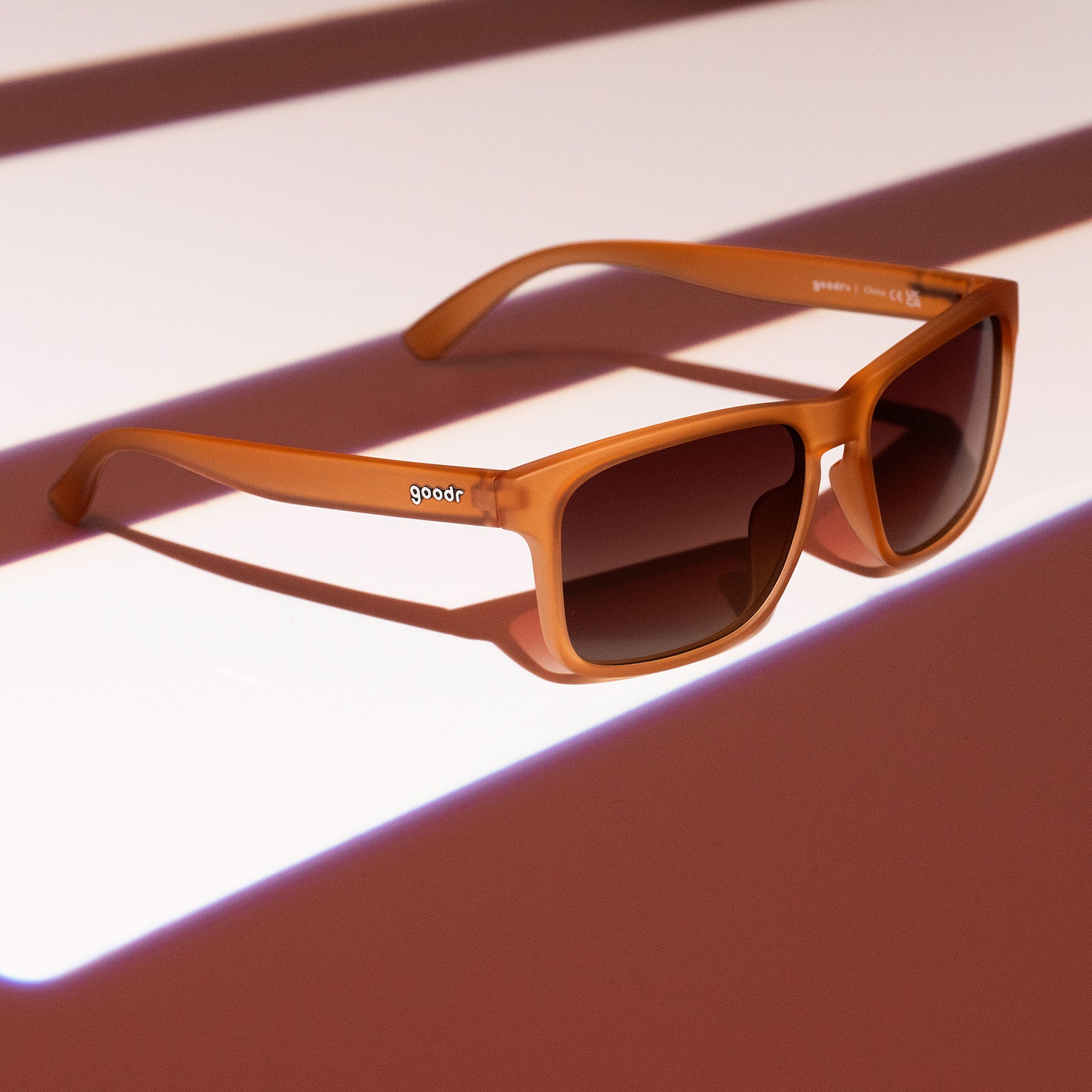 Three-quarter angle view of rich brown Grand Gs with brown-gray gradient lenses on a brown striped surface.