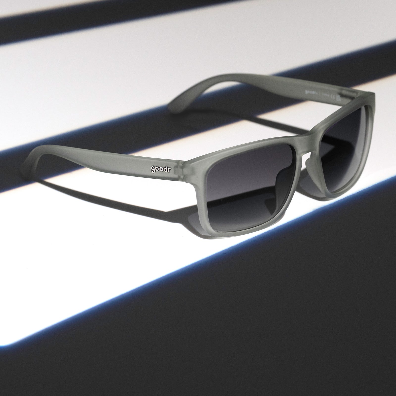 Three-quarter angle view of translucent gray Grand Gs with black gradient lenses on a dark gray striped surface.