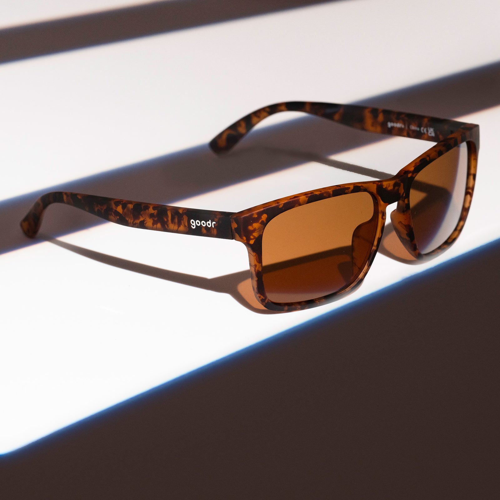 Three-quarter angle view of brown tortoiseshell Grand Gs with brown non-reflective lenses on a striped brown surface.