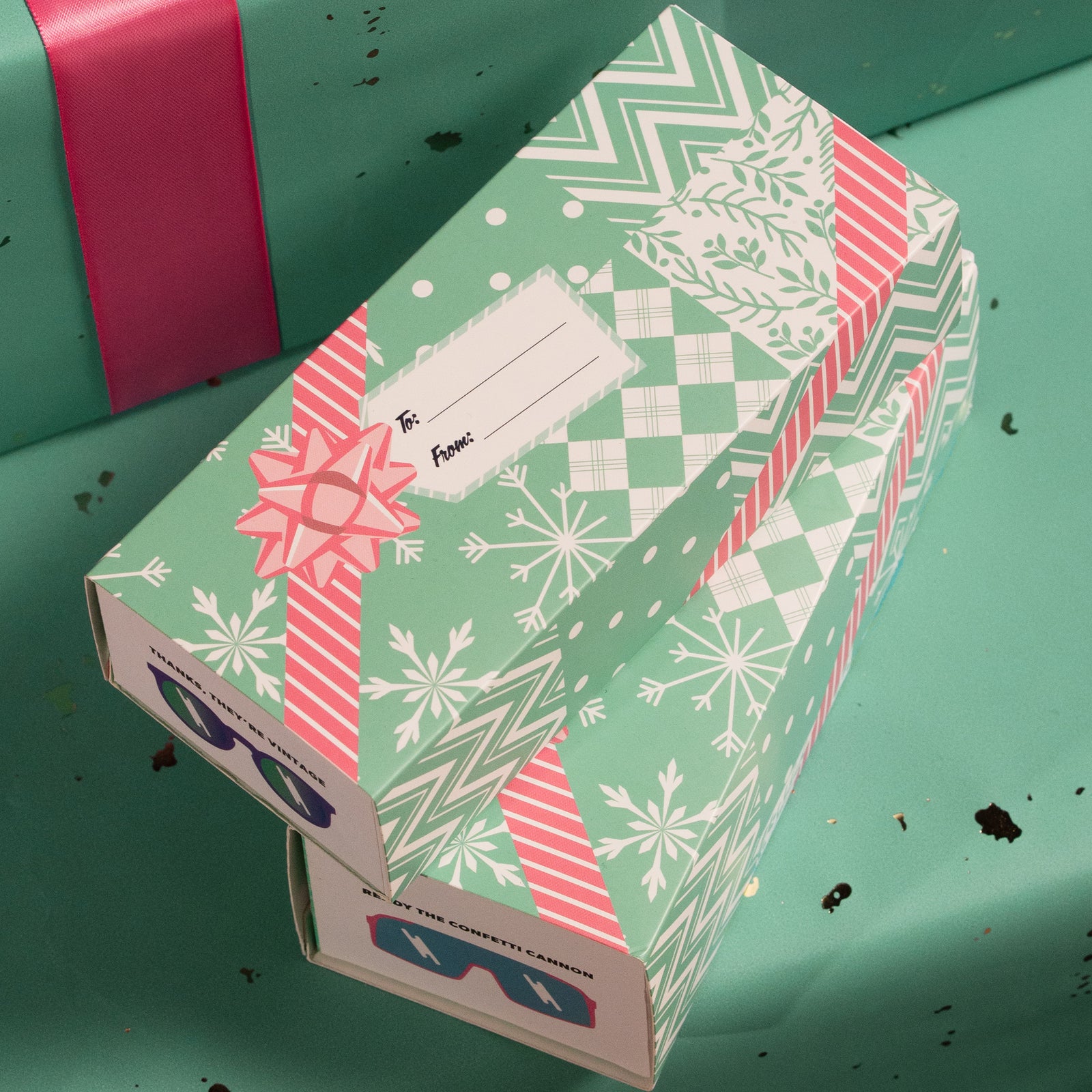 Overhead view of 2 goodr boxes slipped into teal holiday wrapping sleeves featuring a festive pink-and-white holiday design.