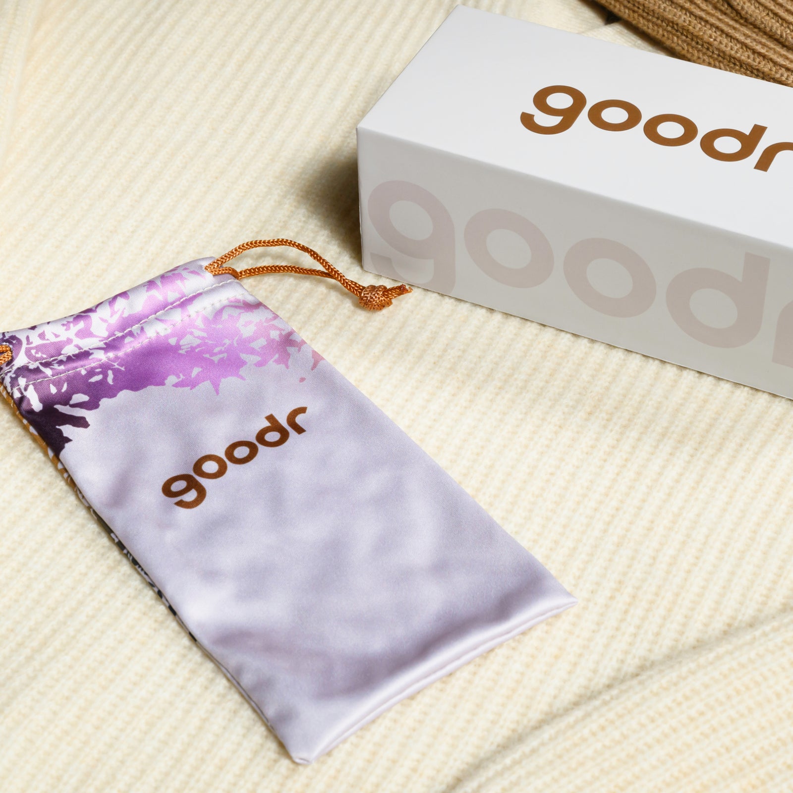 Custom seasonal packaging featuring a pale purple, foliage-inspired microfiber bag resting on cream-colored sweater fabric.