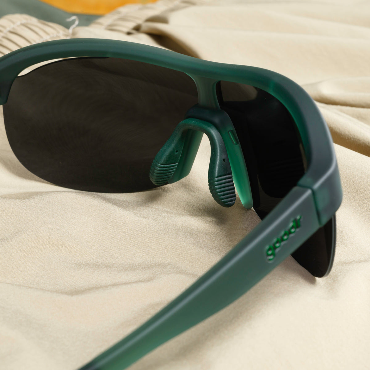 A pair of translucent, dark-green Sonic G sunglasses, photographed from behind, sits on a cream-colored garment.