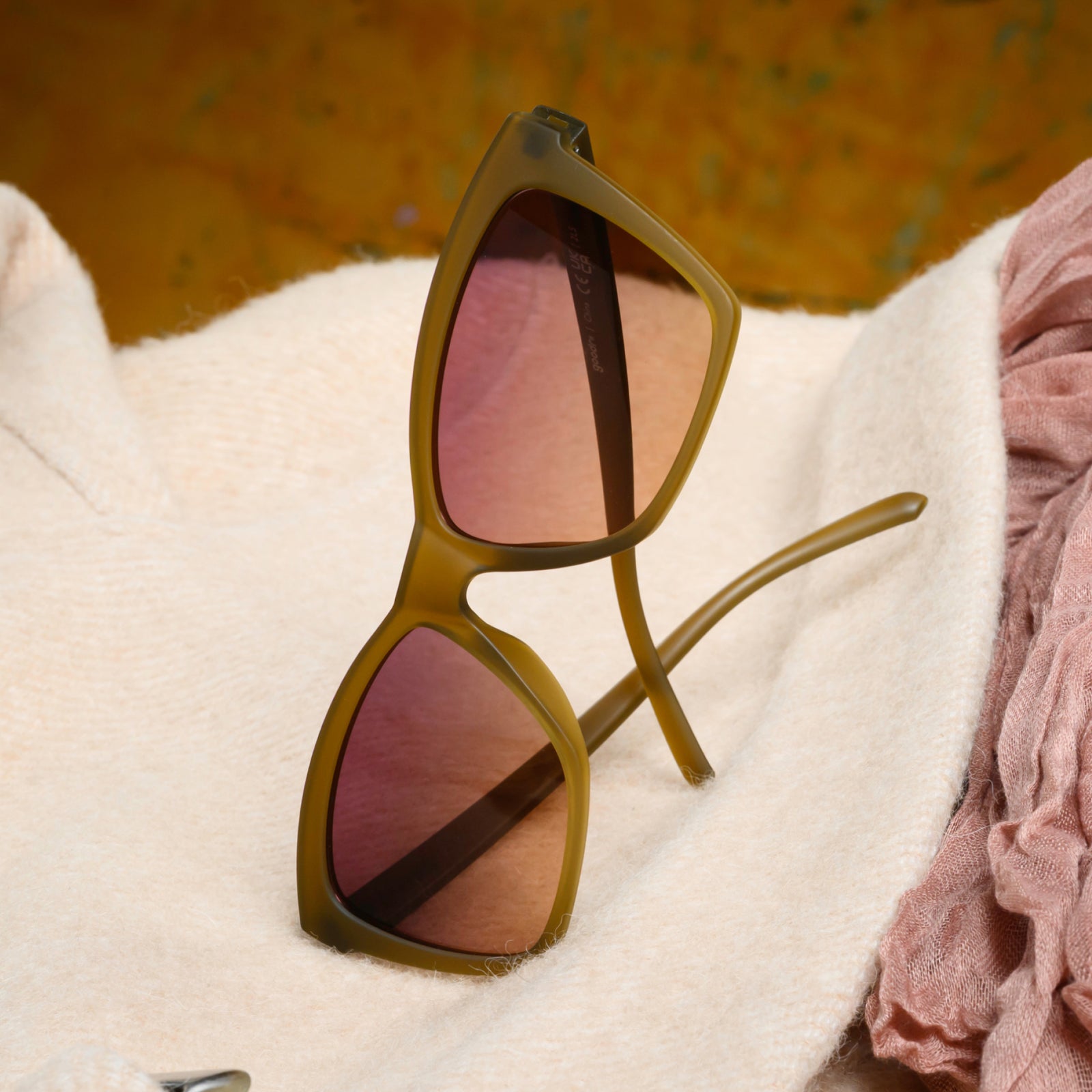 A close-up of a pair of translucent ochre Pop G sunglasses turned on their side, sitting atop a fuzzy cream-colored garment. 