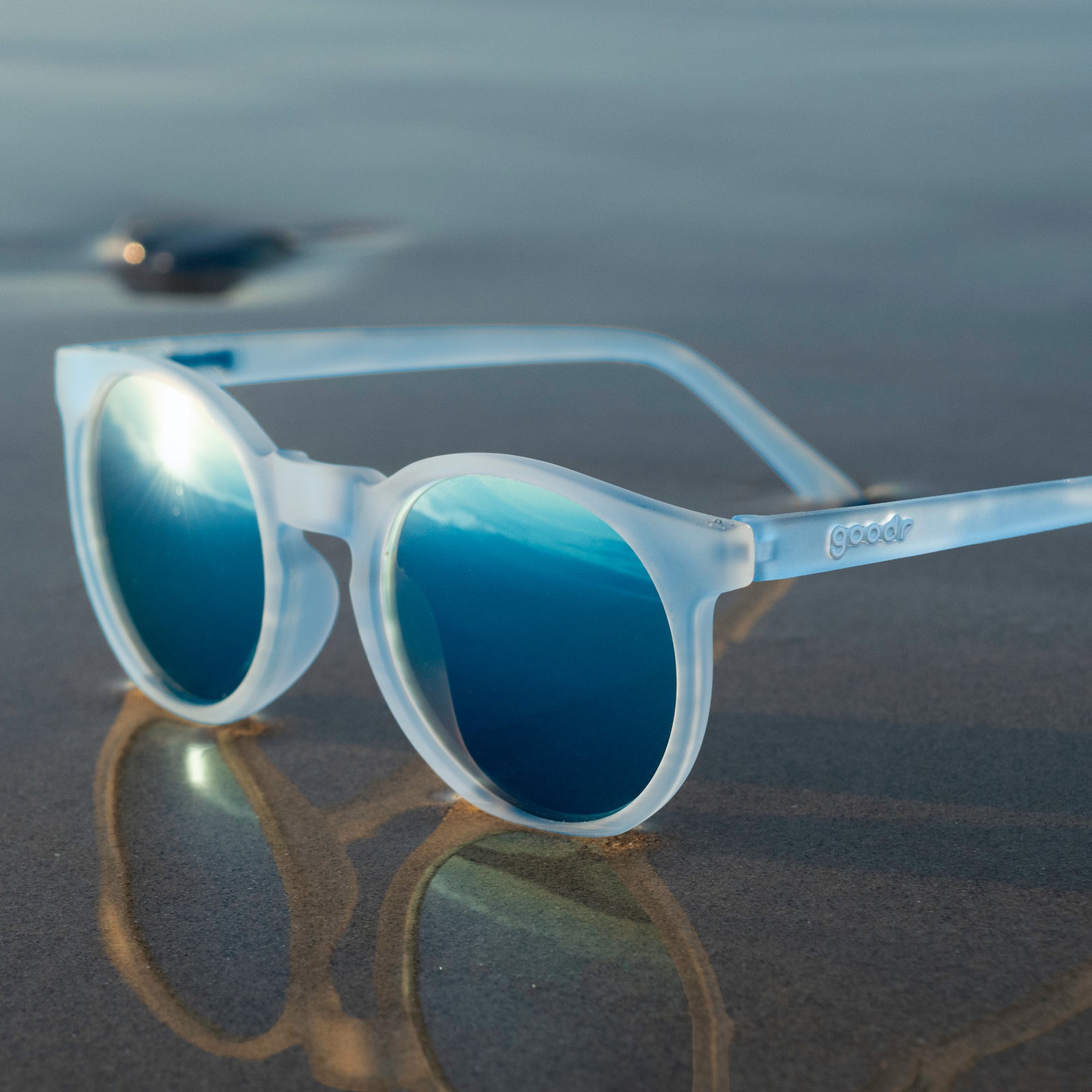 Three-quarter view of translucent blue-gray Circle Gs with ice blue reflective lenses sitting at the wet shoreline.