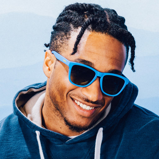 A man smiles while wearing classic blue sunglasses with blue-yellow ocean lenses.