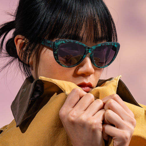 A woman posing while wearing translucent teal tortoiseshell cat-eye frames featuring black gradient lenses.
