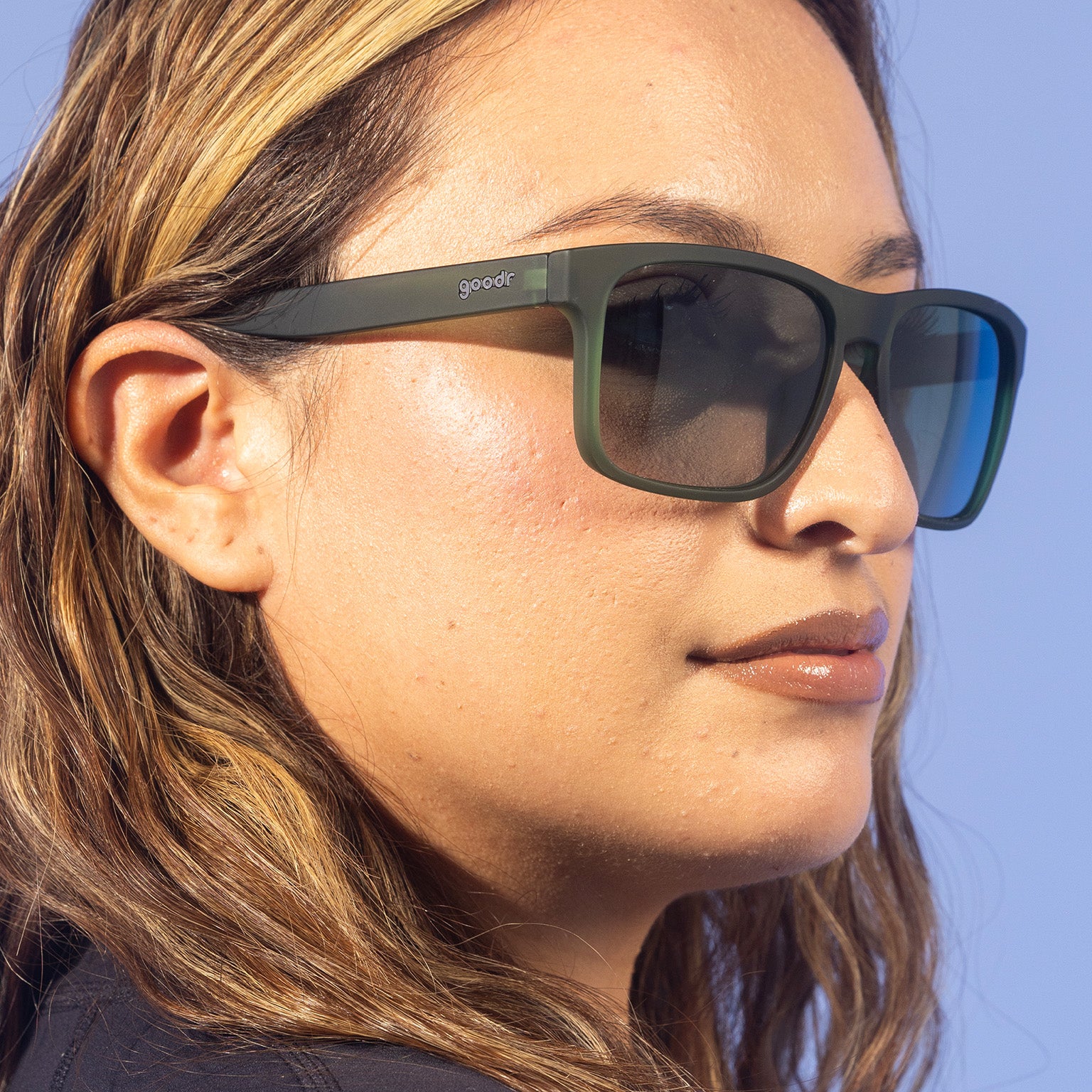 A fashionable woman with wavy blonde hair looks off in translucent dark green Grand Gs with green gradient lenses.