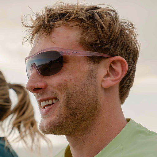 Side profile of a man running and smiling while wearing translucent purple wrap shield sunglasses with gradient purple lenses.