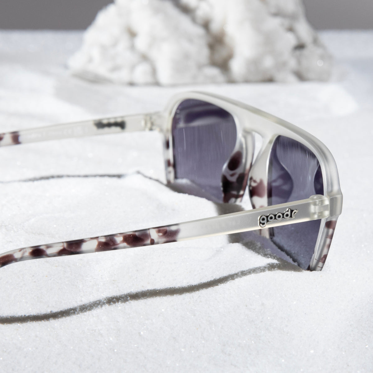 Translucent light gray retro aviator sunglasses with a tonal pattern sit folded and resting on snow.