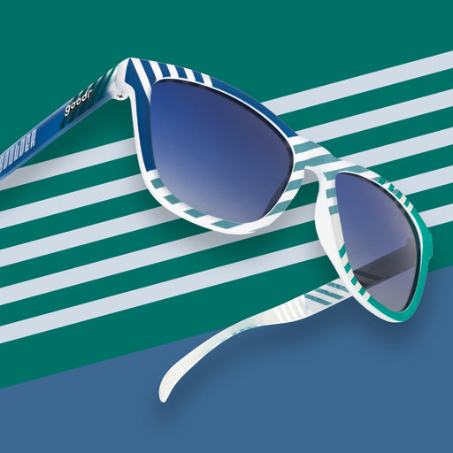 Right three-quarter angle view of blue and green striped sunglasses with blue gradient lenses in front of a striped background.