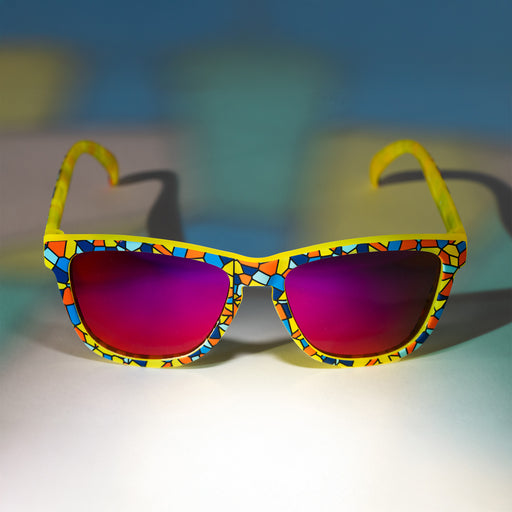 A pair of colorful sunglasses with a stained glass design sits on a white background with a stained glass lighting effect.