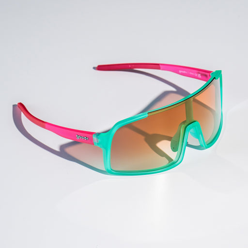 Three-quarter view of teal wrap sunglasses with amber gradient lenses sitting on a white surface.