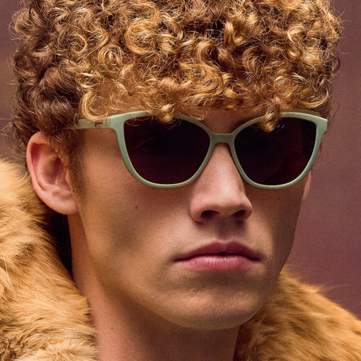 Person wearing sunglasses and a fur-lined hood against a brown background