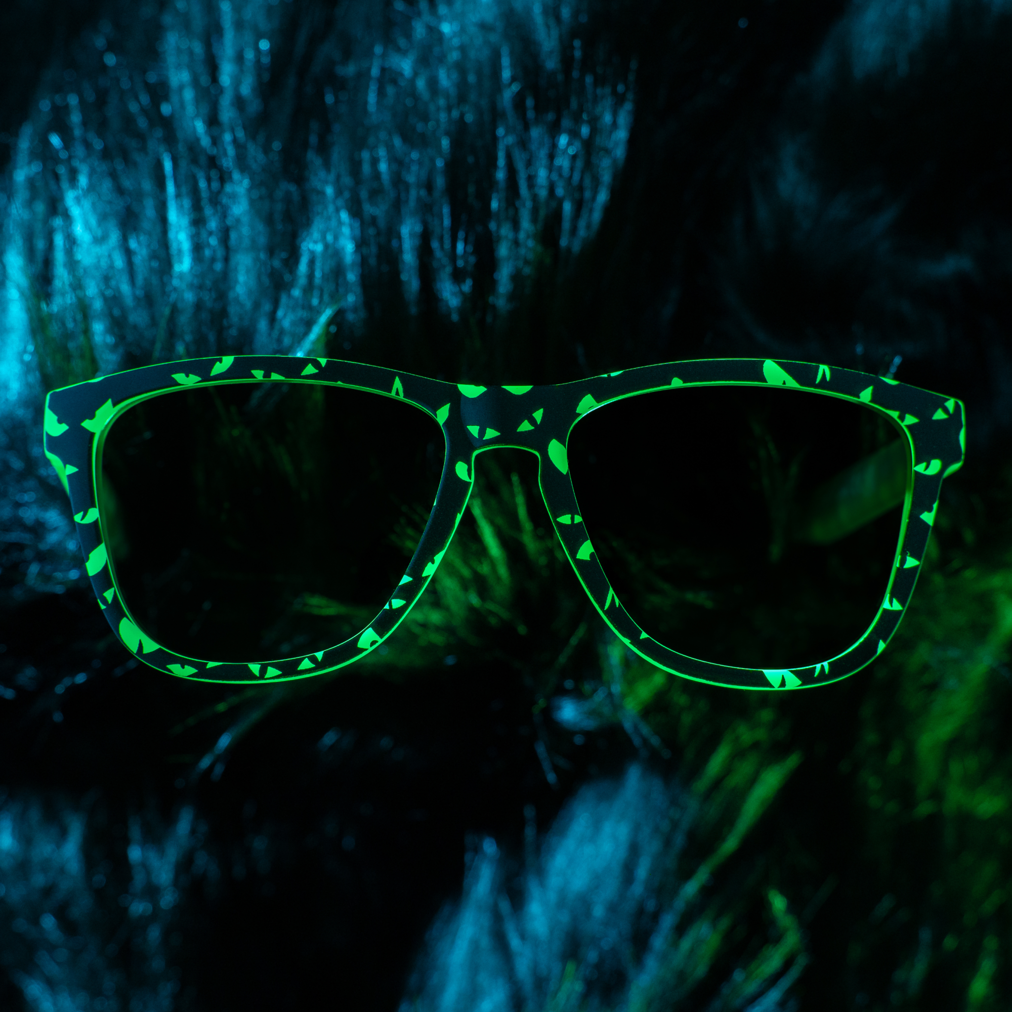A pair of spooky glow-in-the-dark sunnies with a glowing-eyes design is folded on a dark fur backdrop.