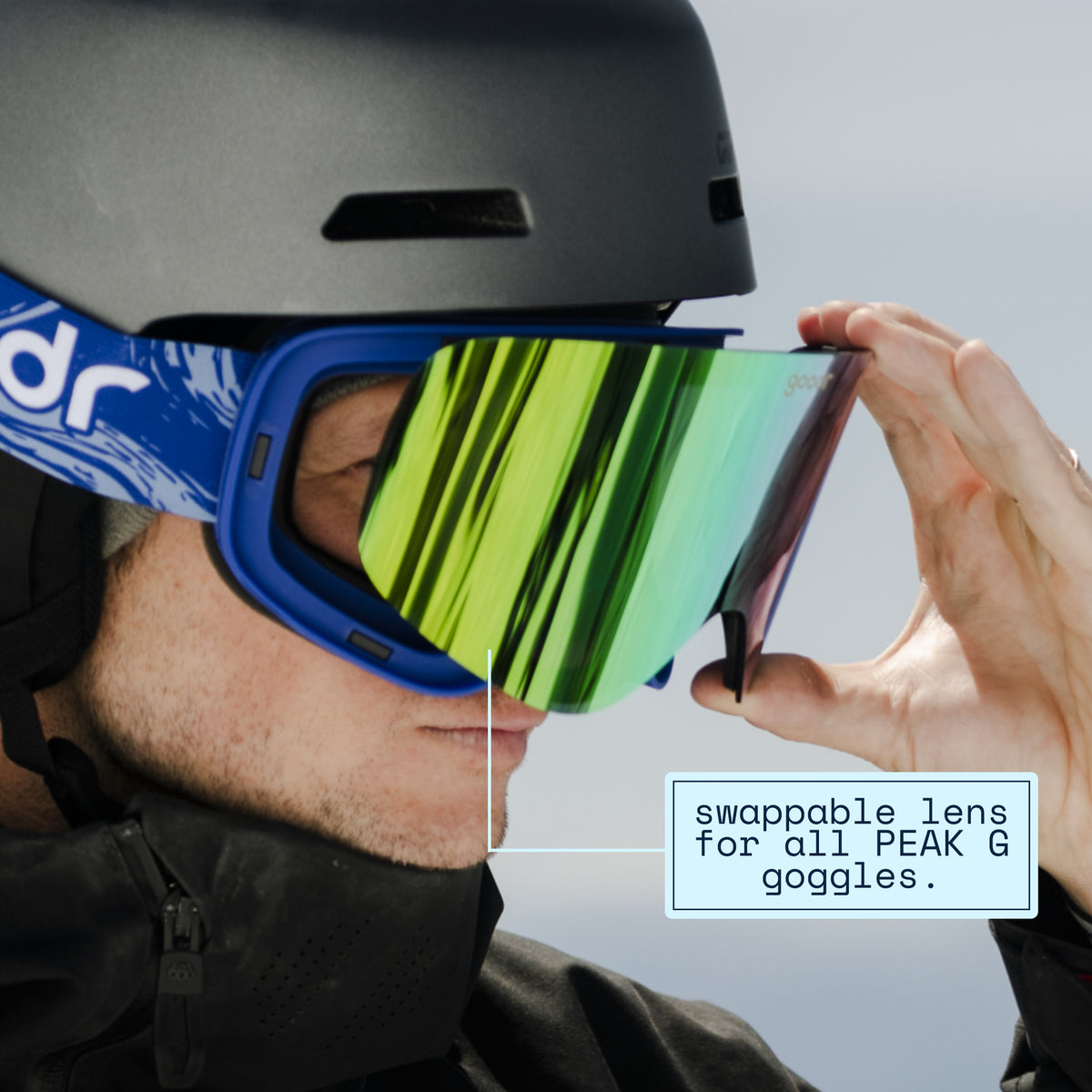 Skier swapping a green mirrored replacement lens onto blue goodr ski goggles.