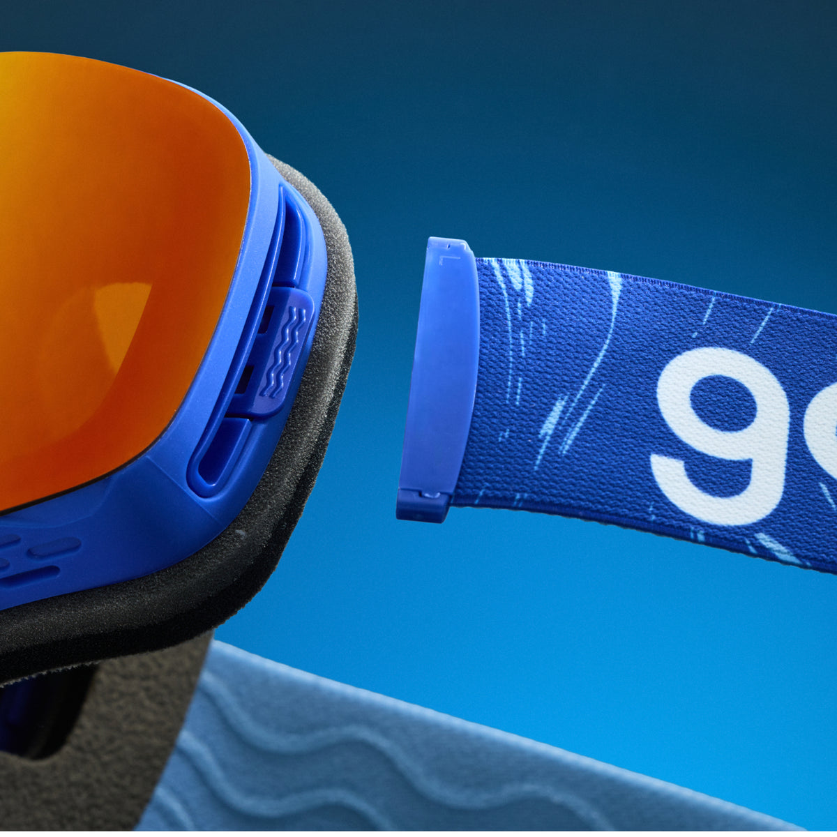 Close-up of bronze red mirrored snow goggles with a detachable blue goodr strap.