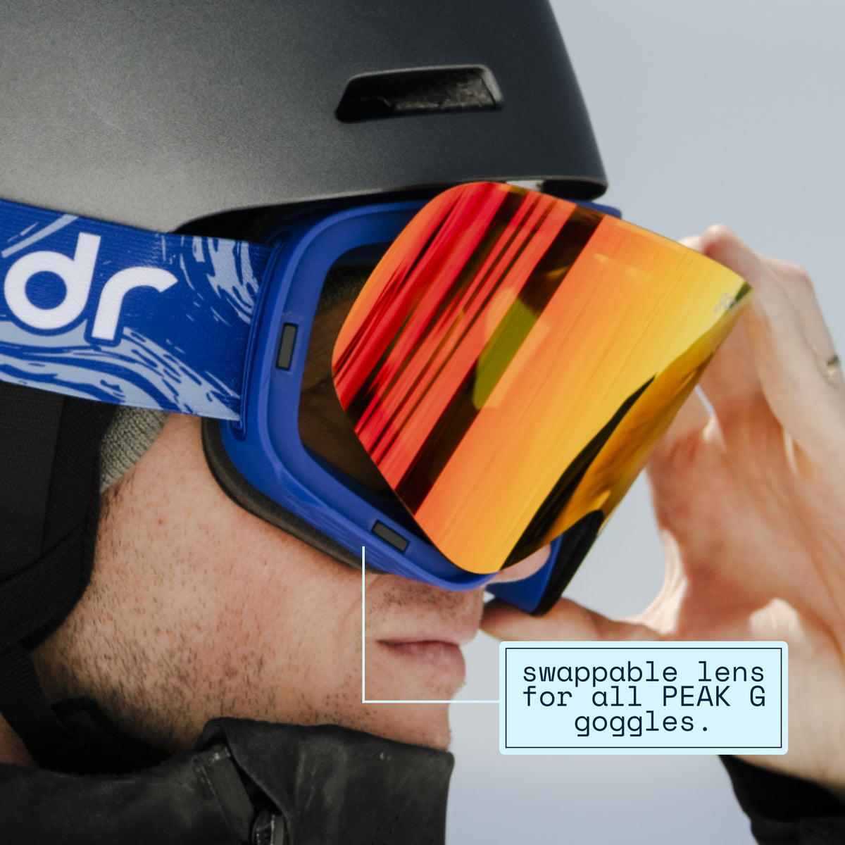 Skier swapping a pink mirrored replacement lens onto blue goodr ski goggles.