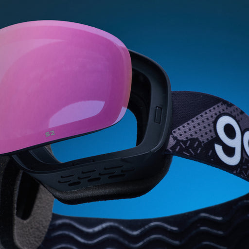 Pink replacement lens resting above black goodr ski goggles.