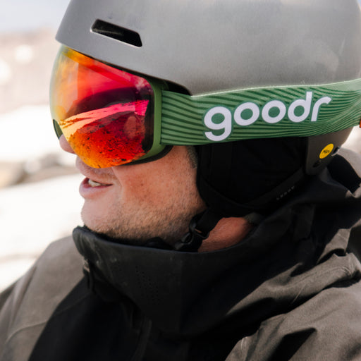 Skier wearing smoke red mirrored snow goggles with a green goodr strap and gray helmet.