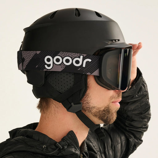 Skier wearing black snow goggles with a patterned goodr strap and black helmet.