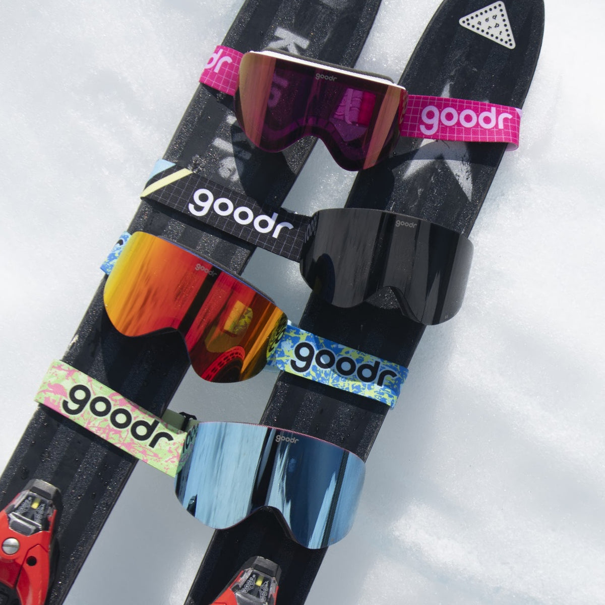 Black goodr goggle strap shown on ski goggles alongside other colorful goggles on snow.