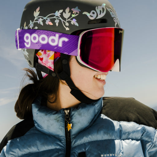 Skier wearing purple red mirrored snow goggles with a purple goodr strap and black helmet.
