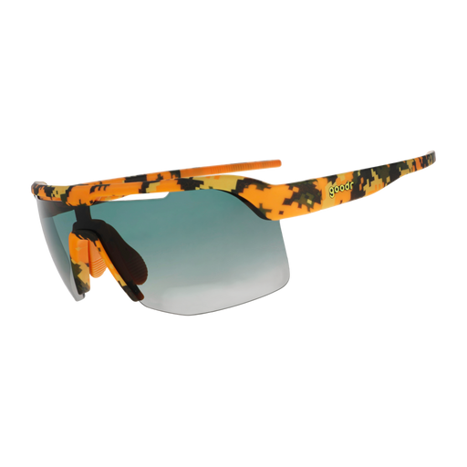 Sport sunglasses with a vibrant orange, yellow, and black camouflage pattern on the frame and arms, featuring a blue-to-gray gradient lens and a small green 'goodr' text logo on the temple.