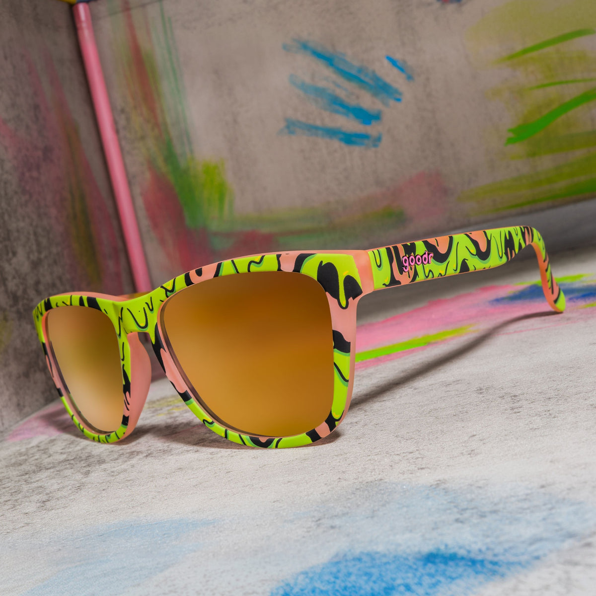 Pink sunglasses with gold lenses and a gooey green-and-black slime pattern on a colorful painted set.
