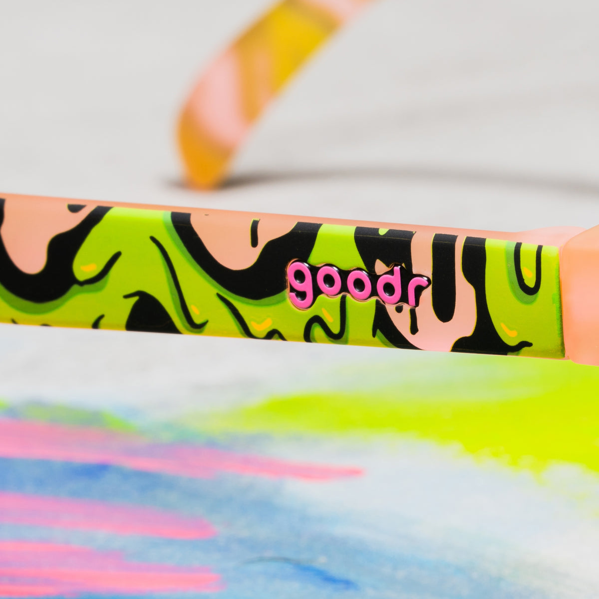 Close-up of the goodr logo on a pink sunglasses arm with a gooey green-and-black slime pattern.